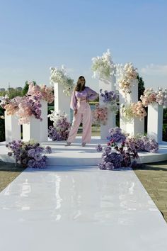 a woman is standing in front of a white sculpture with pink and purple flowers on it