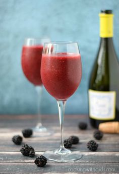 two glasses filled with raspberry wine next to a bottle of wine and some blackberries