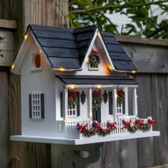 a white birdhouse with christmas decorations and lights on it's roof next to a wooden fence