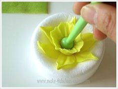 a hand holding a green plastic object in the shape of a flower on top of a white surface