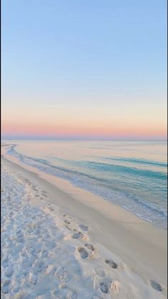 the beach is covered in white sand and footprints leading into the water at sunset or dawn