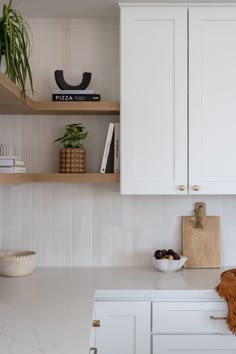 a kitchen with white cupboards and shelves filled with fruit, vegetables and other items