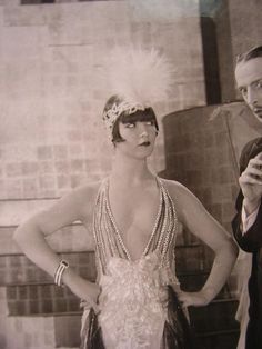 a man standing next to a woman in a flap dress and feathered headpiece