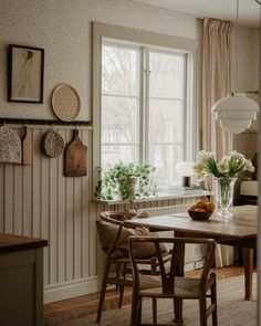 a dining room table and chairs with flowers in vases on the window sill