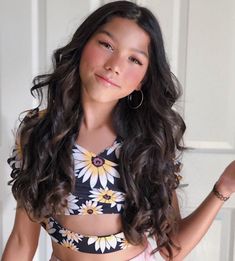 a woman with long dark hair wearing a flowery top and holding her hands out