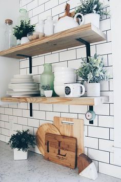 a kitchen shelf filled with pots, pans and cutting boards on top of a white tiled wall