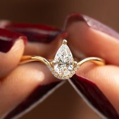 a close up of a person's hand holding a ring with a pear shaped diamond