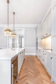 an empty kitchen with white cabinets and wood flooring on the walls, along with a chandelier hanging from the ceiling