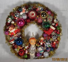 a christmas wreath with ornaments hanging from it's sides and a doll in the middle