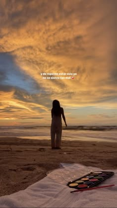 a woman standing on top of a sandy beach next to the ocean under a cloudy sky