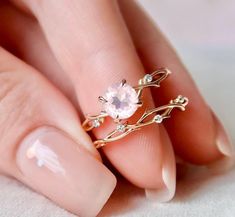 a woman's hand holding a ring with an oval pink stone in the middle