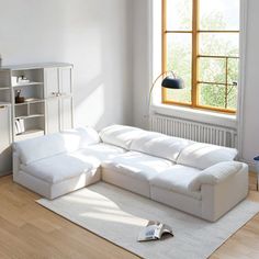 a living room with a large white couch and book shelf in the corner next to a window