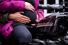 a pregnant woman sitting on the back of a motorcycle while holding her baby bumping it's belly