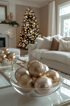 a glass bowl filled with gold ornaments on top of a table next to a christmas tree