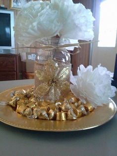 a gold plate topped with white flowers and chocolates next to a vase filled with paper pom poms