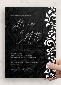 a hand holding up a black and white wedding card with an ornate design on it