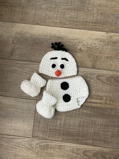 a crocheted snowman hat and mittens sitting on a wood floor,