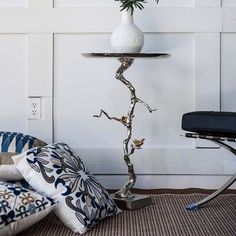 a white vase with flowers sitting on top of a table next to a chair and ottoman