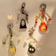 four different key chains with charms attached to them on a white surface, one has an emoticive face and the other has a cartoon character