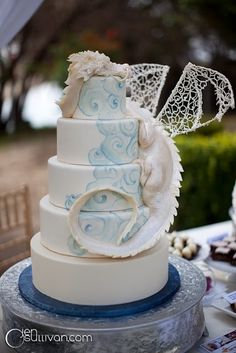 a three tiered wedding cake with blue and white designs on the top, sitting on a table