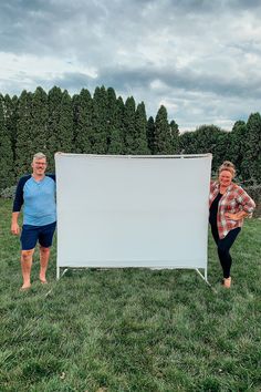 two people standing in front of a large white board on the grass with trees behind them