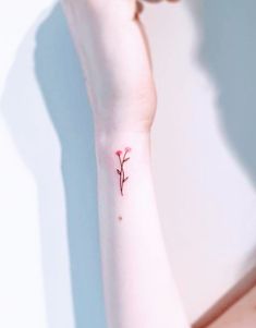 a woman's wrist with a small red flower tattoo on the left side of her arm