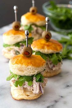 mini sandwiches with olives and lettuce are on a marble countertop, ready to be eaten