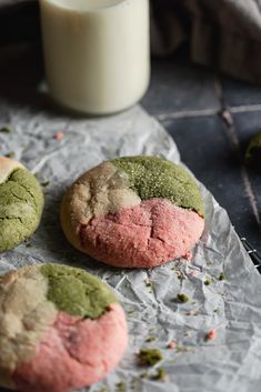 three cookies with green and pink frosting next to a glass of milk on a table