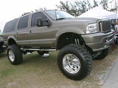 a large gray truck parked next to other trucks in a field with tents behind it