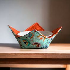 an orange and white paper boat sitting on top of a wooden table next to a wall