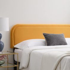 a yellow headboard on a bed with white sheets and pillows, next to a night stand