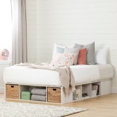 a white bed with drawers underneath it in a room next to a rug and window