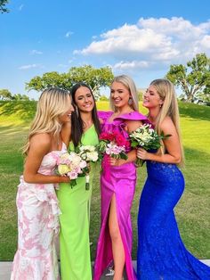 four beautiful young women standing next to each other in formal dresses and holding bouquets