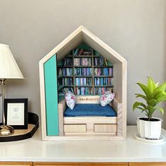 a dollhouse bed made out of bookshelves on a desk with a lamp and potted plant