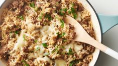 a skillet filled with meat and rice topped with parsley on the side next to a wooden spoon