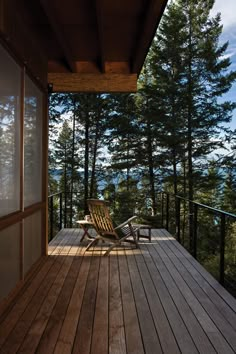 a wooden deck with two chairs on it and trees in the backgrouund