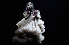 a woman with long hair and makeup in a white dress standing on a black background