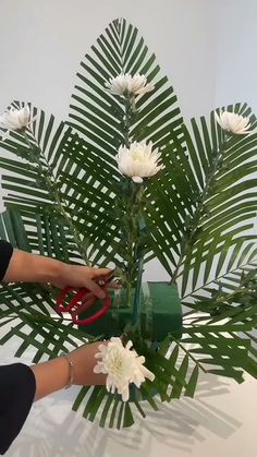 a woman is using scissors to cut flowers in a vase with palm leaves on the table