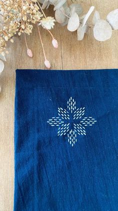 a blue table cloth with an embroidered flower on it and some flowers in the background