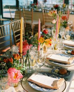 a long table set with place settings, candles and flowers in vases on it