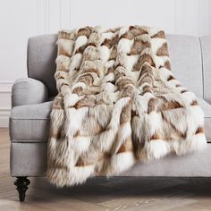 a grey couch with a brown and white fur blanket on it's back next to a wooden floor