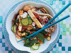 a white bowl filled with rice and vegetables next to chopsticks on a blue checkered table cloth