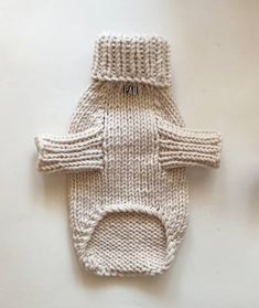 a white knitted dog sweater laying on top of a table