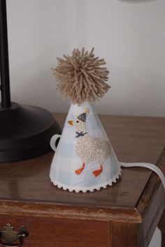 a party hat with a sheep on it sitting on top of a wooden table next to a lamp