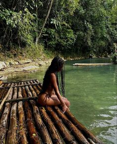 a woman sitting on top of a bamboo raft in the middle of a river surrounded by trees