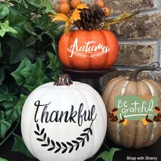 three painted pumpkins sitting next to each other on top of a black table with greenery