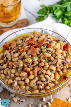 a glass bowl filled with beans and bacon on top of a wooden table next to some parsley