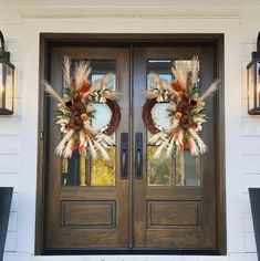 two wreaths are on the front door of a house with lanterns hanging above them