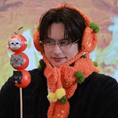 a woman with glasses and a knitted scarf around her head holding an orange cat lollipop