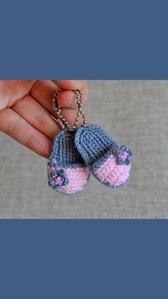 a hand holding two small knitted baby shoes on a chain with pink and blue beads